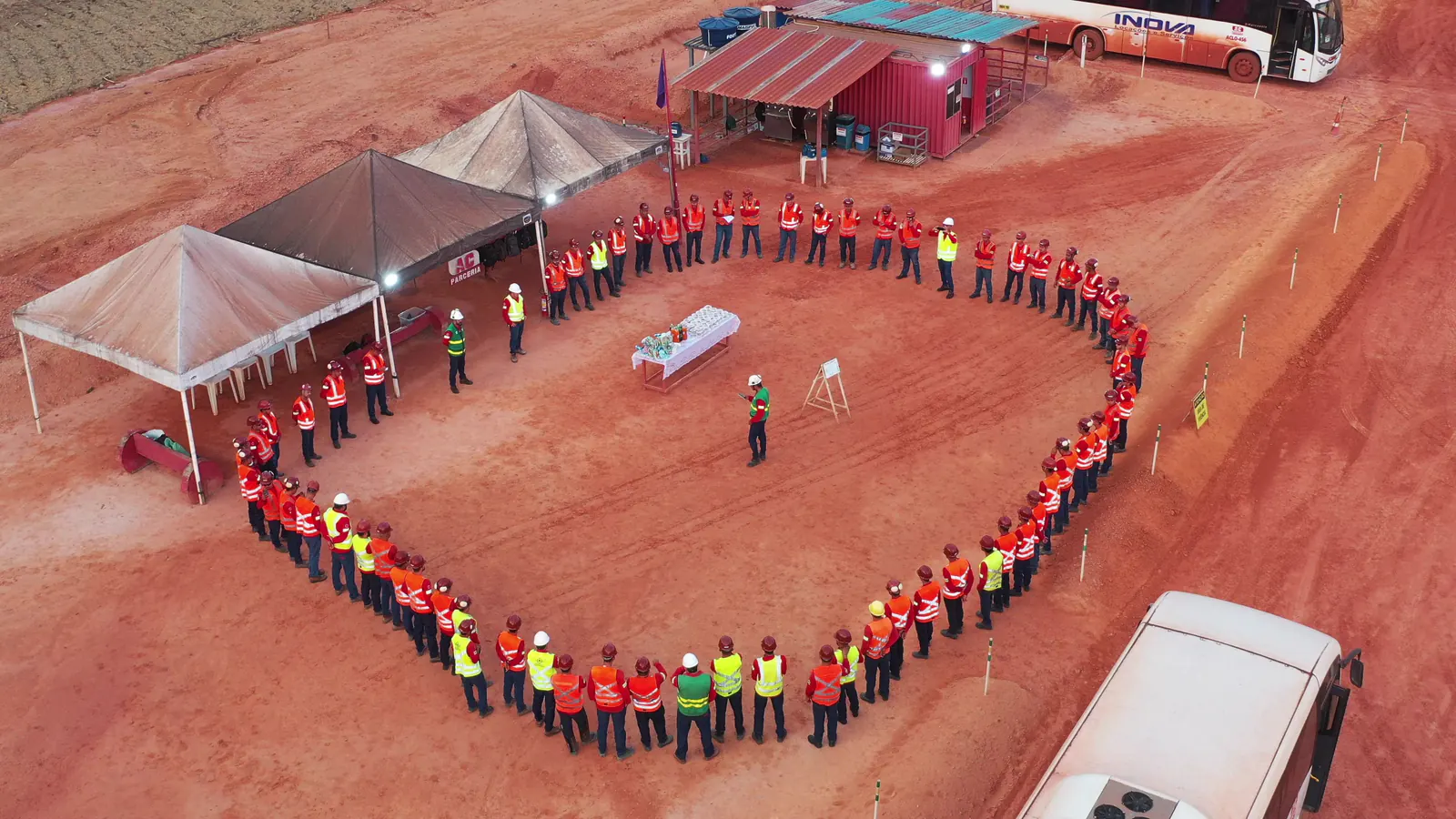 Equipe da AC, de uniforme vermelho e EPI, reunida em roda para o diálogo de segurança, vista do alto