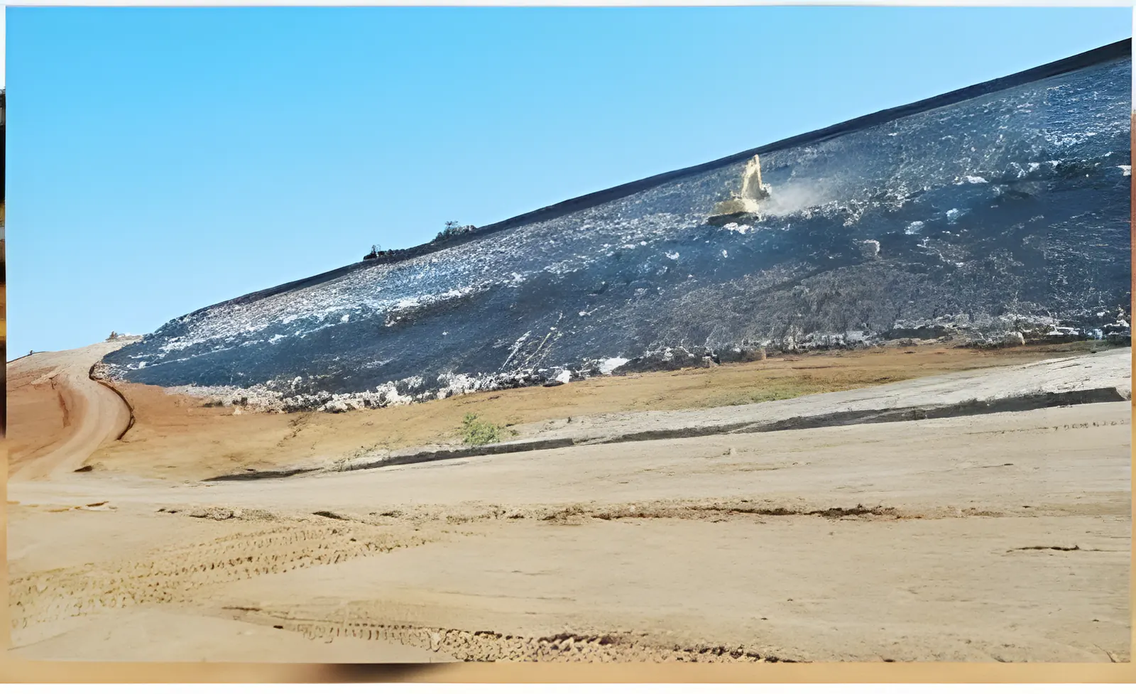 Talude de barragem revestido com manta escura, sob céu azul
