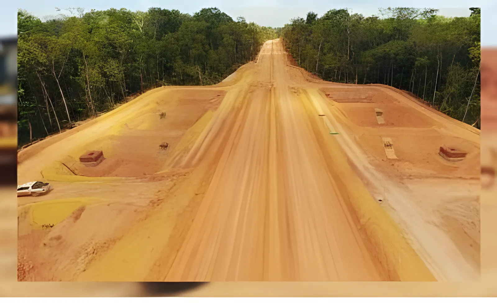 Estrada de terra larga e reta aberta em meio à floresta