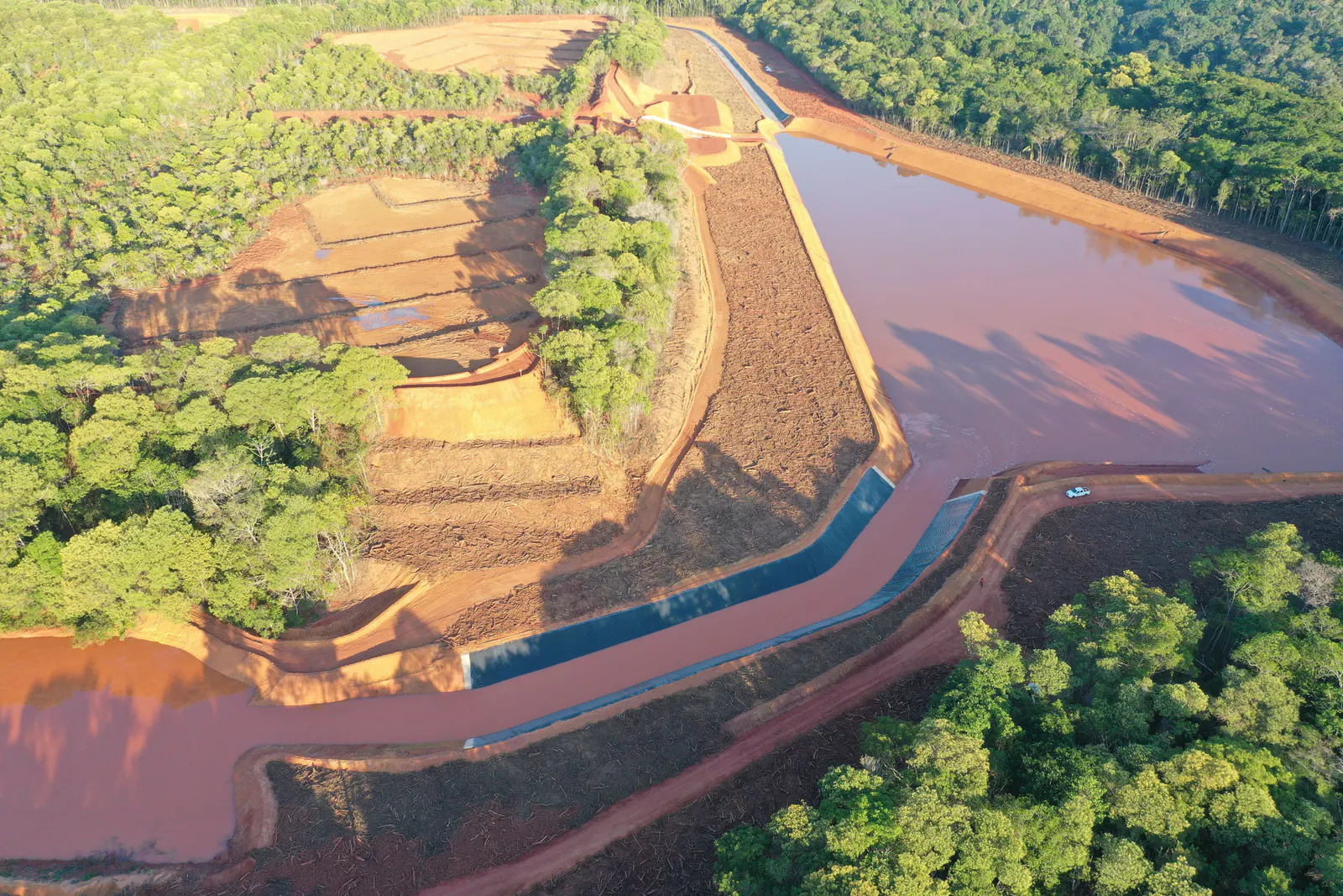 Reservatório de água avermelhada com talude em bancadas e canal revestido