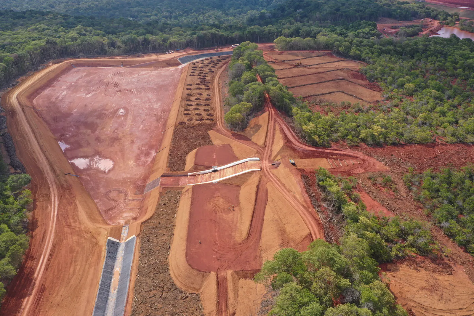 Vista aérea de canal de drenagem cortando área em recuperação, com floresta ao redor