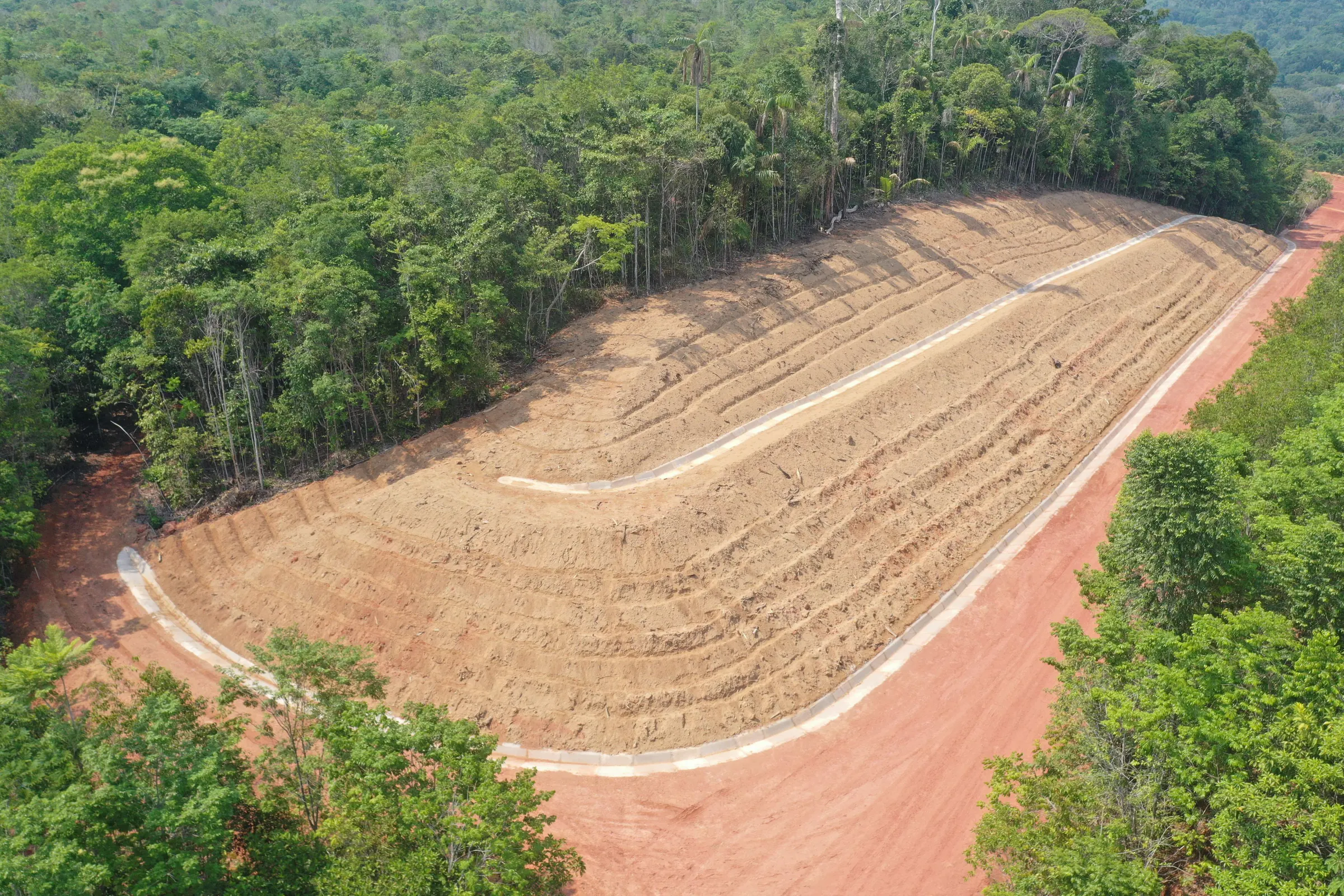 Vista aérea de talude conformado em bancadas, com canaletas de drenagem, no meio da floresta densa