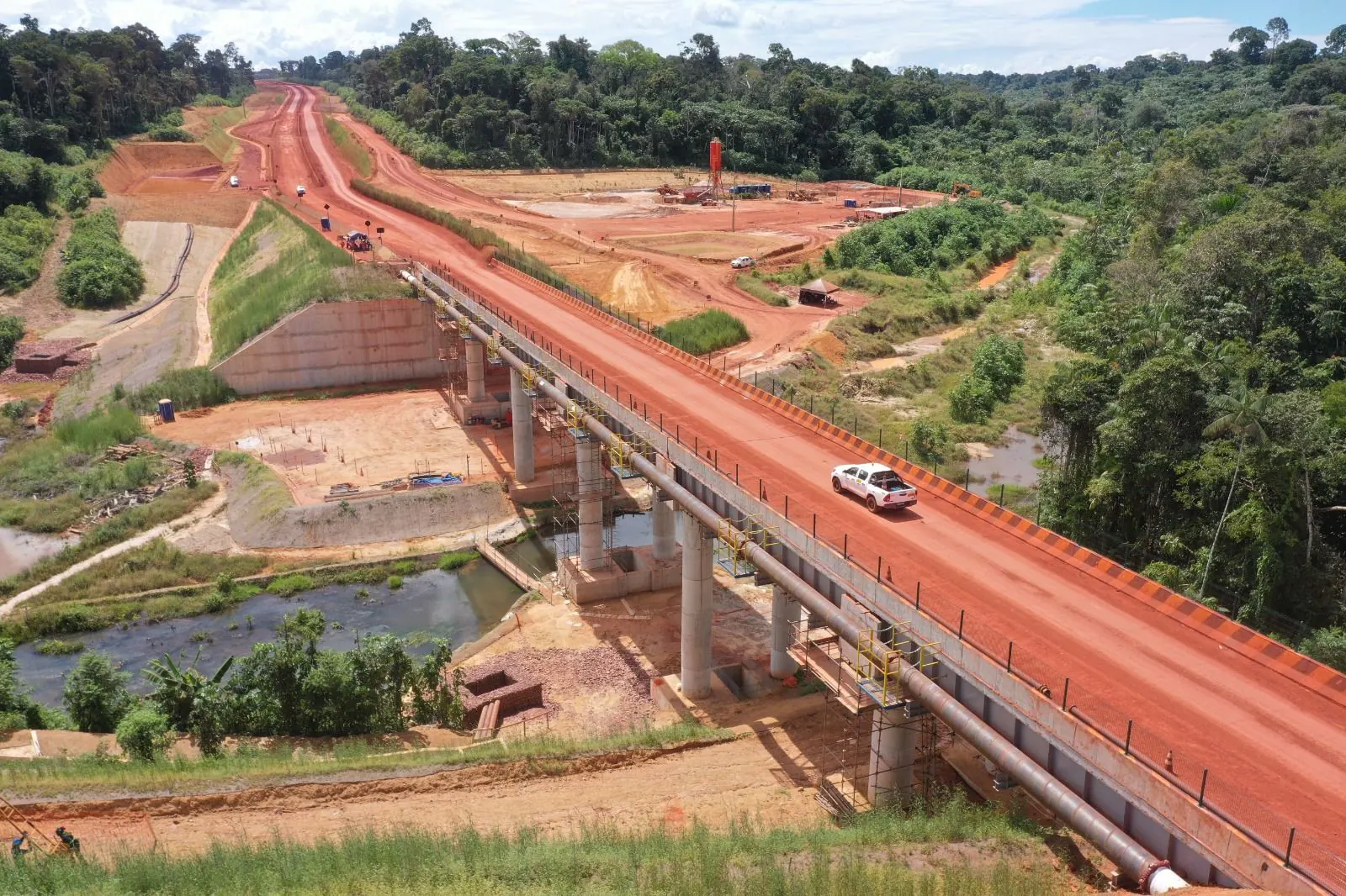 Vista aérea da Estrada AWA: ponte em concreto sobre igarapé, estrada de terra vermelha e floresta ao redor